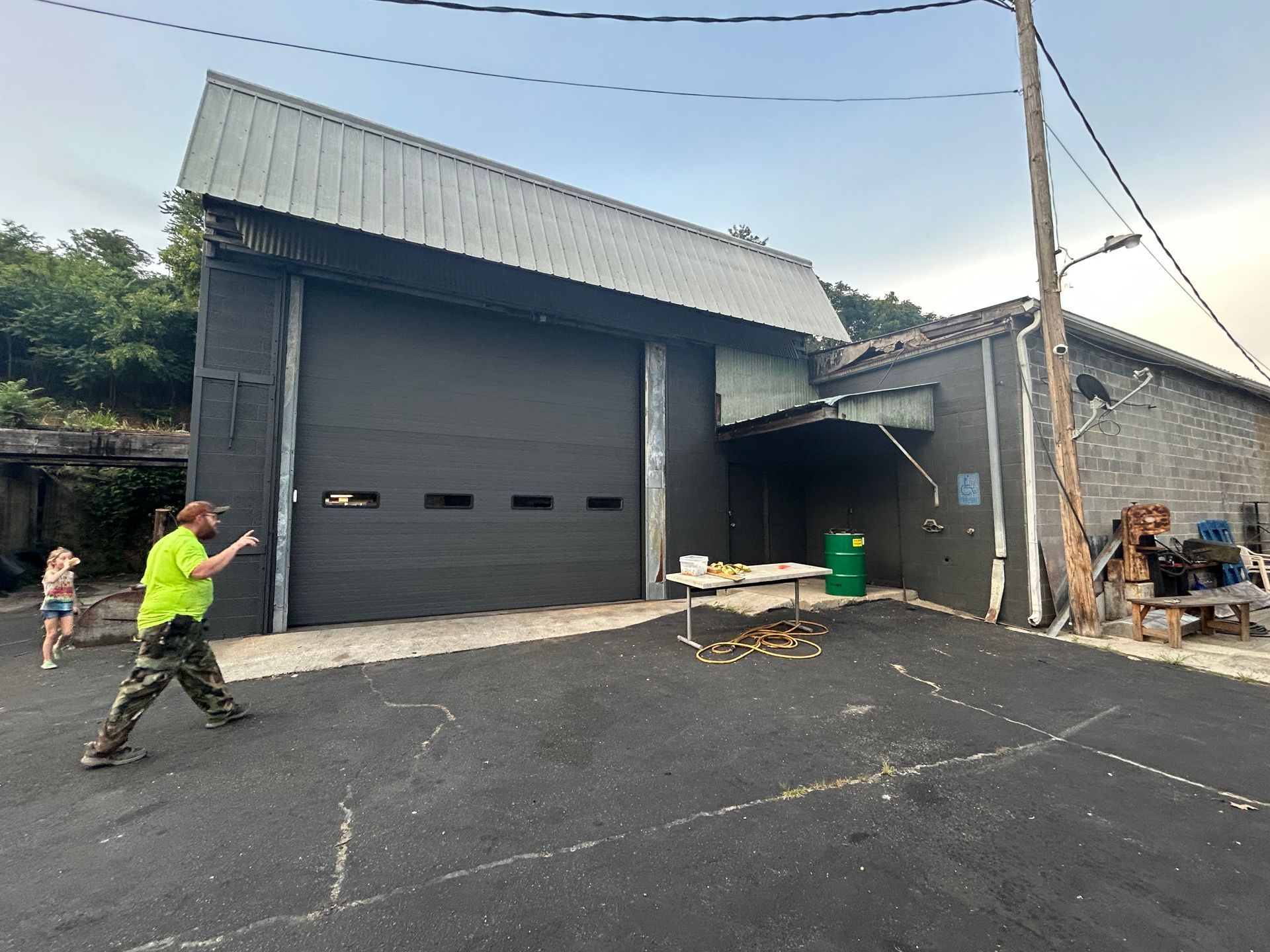 Man and child near a dark garage building with a closed door, outdoors.