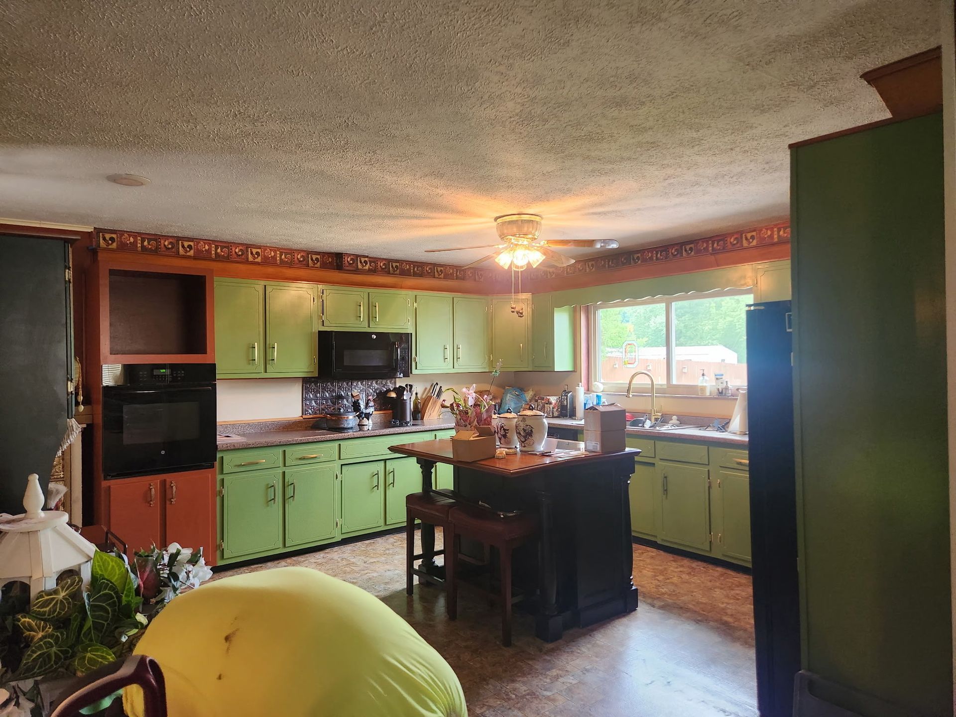 Green kitchen with black appliances, a wooden island, and an ornate ceiling light.