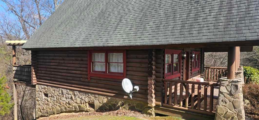 Log cabin with a stone foundation and red-framed windows and doors.