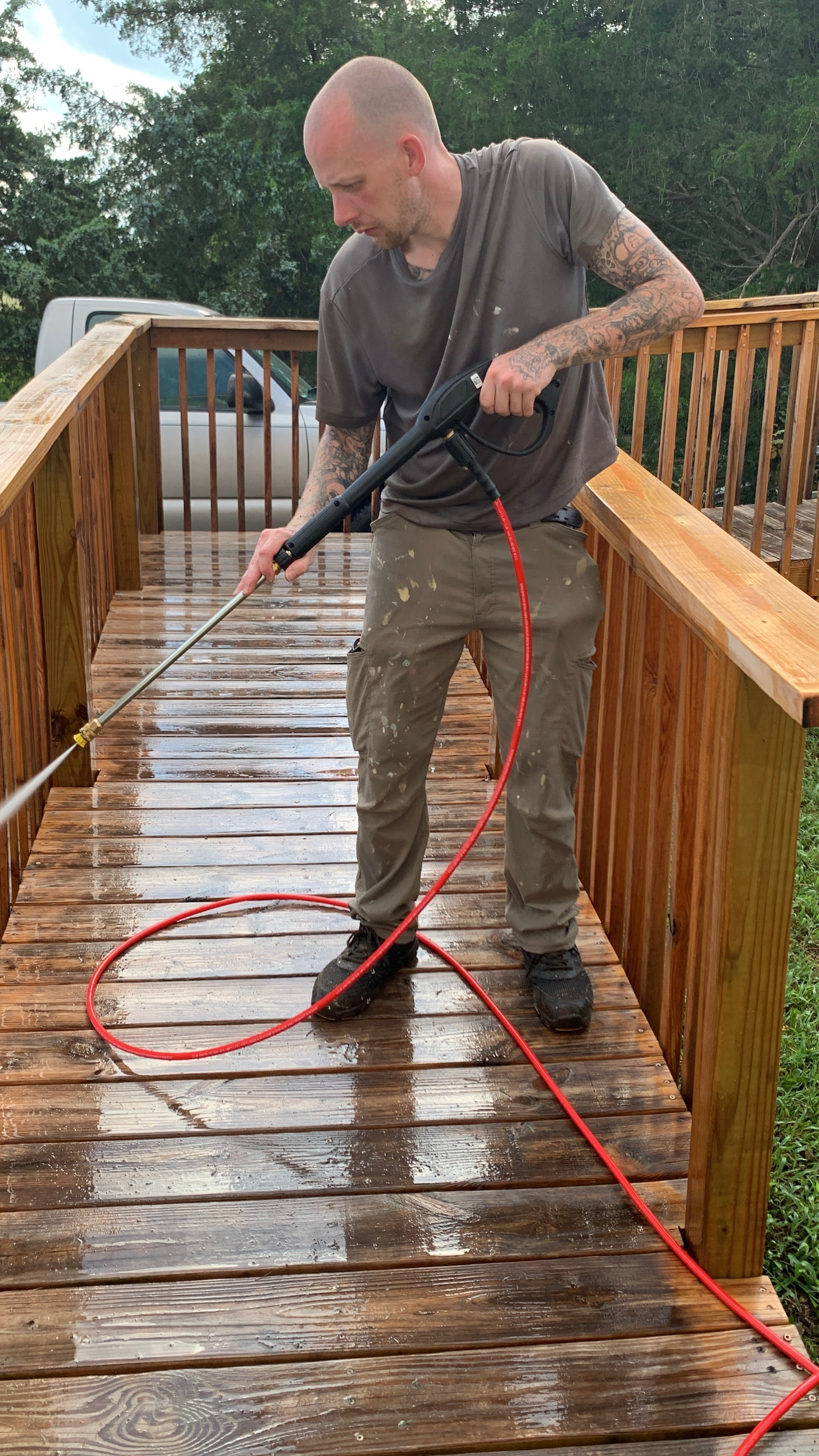 Man power washing a wooden deck with a pressure washer; outdoors.