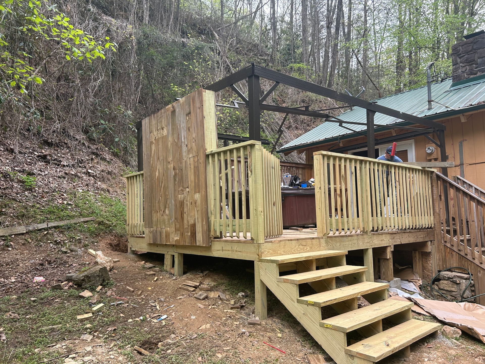 Wooden deck with stairs, built-in hot tub, and pergola, set against a wooded hillside.