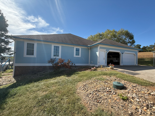 Man on ladder applying sealant to log cabin window frame.