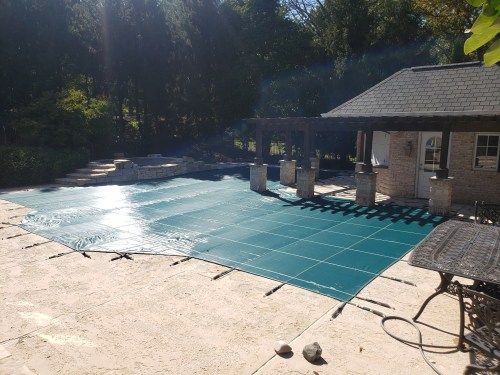 A large swimming pool with a green cover and a house in the background.