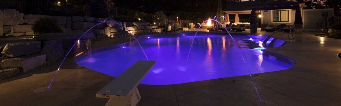 A large swimming pool is lit up at night with purple lights.