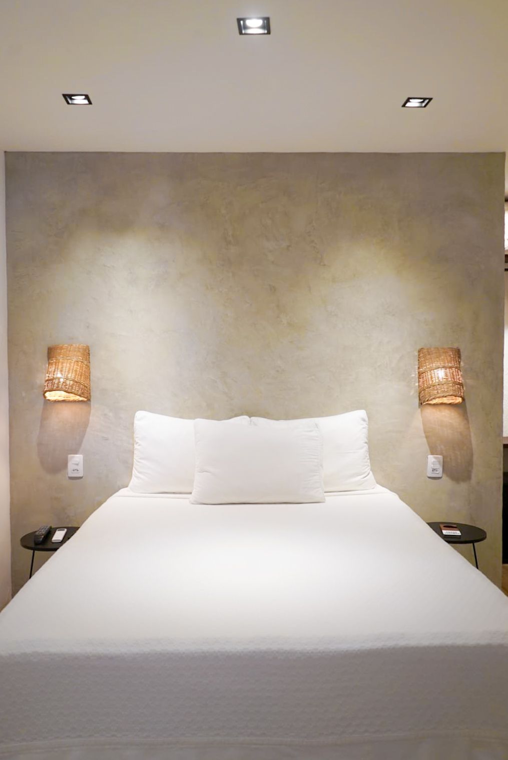 Bedroom with bed, neutral-toned textured wall, sconce lighting, white bedding, and recessed ceiling lights.