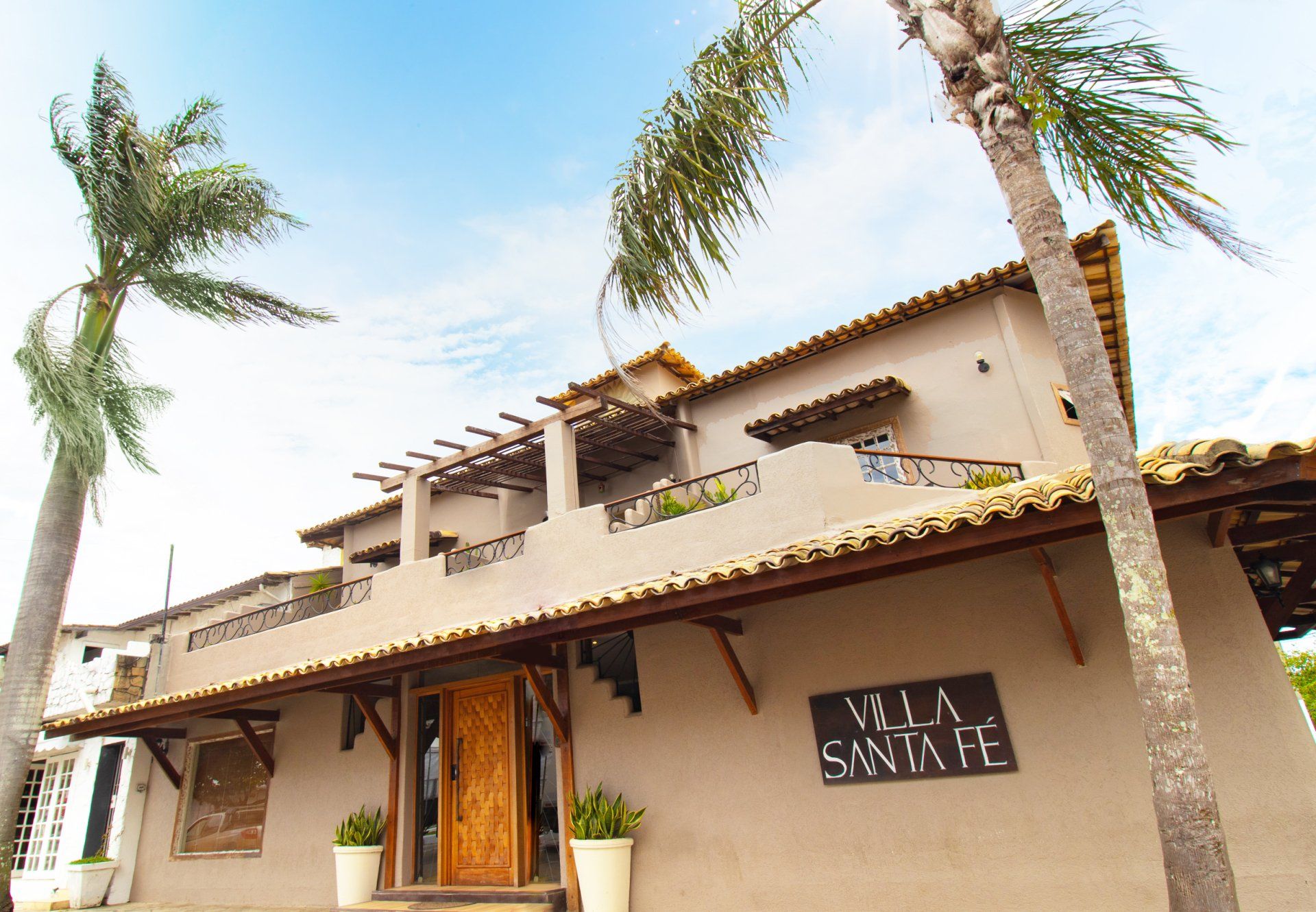 Villa Santa Fe building with palm trees against a cloudy sky. The building is light brown.