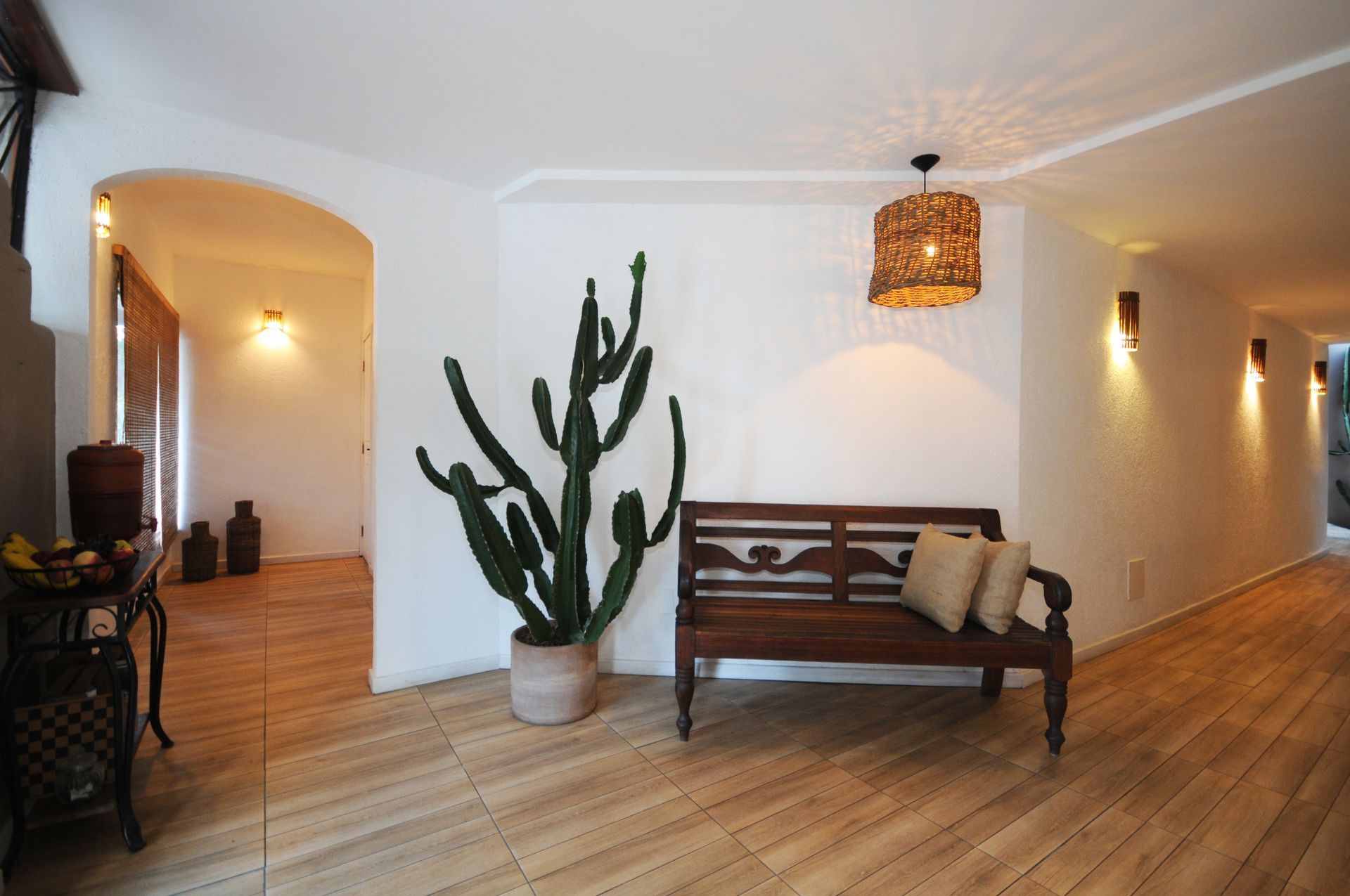 Hallway with bench, cactus, arched doorway, wood flooring, and decorative lighting.