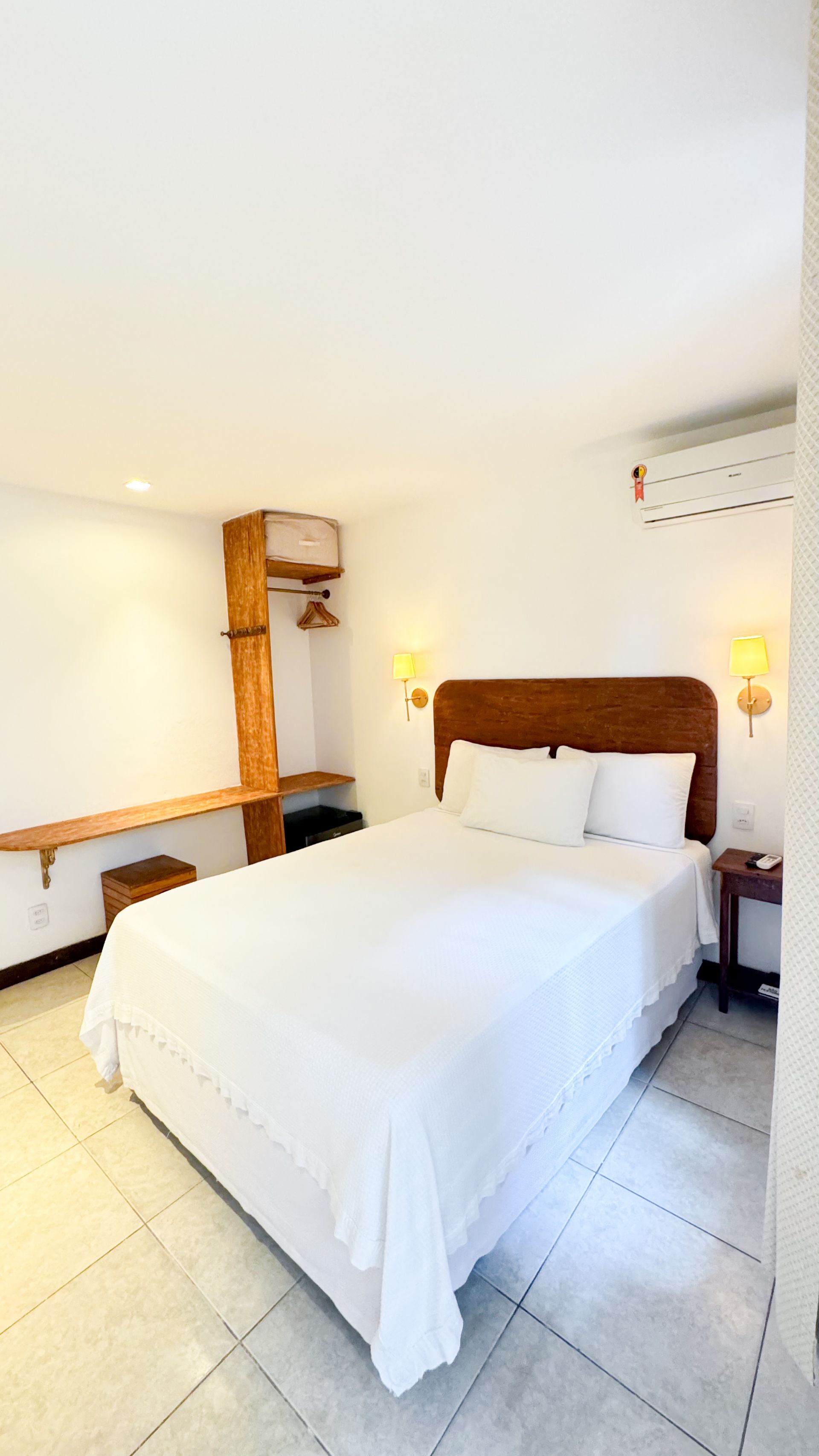 Bedroom with white bed, wooden headboard, small nightstand, and wardrobe against white walls.