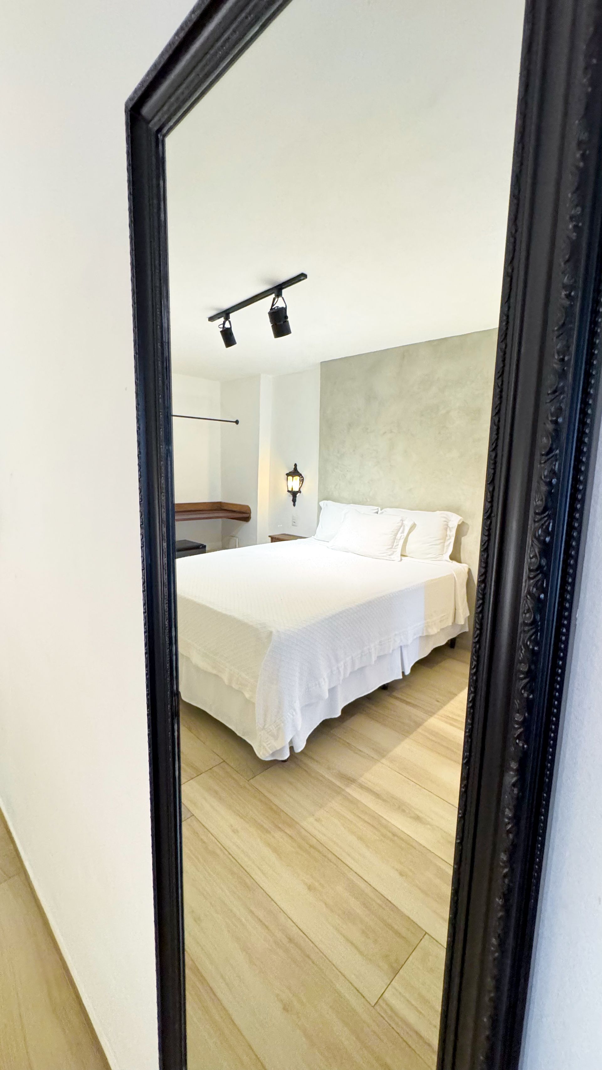 Mirror reflecting a bedroom with a bed, light wood floors, and textured accent wall.