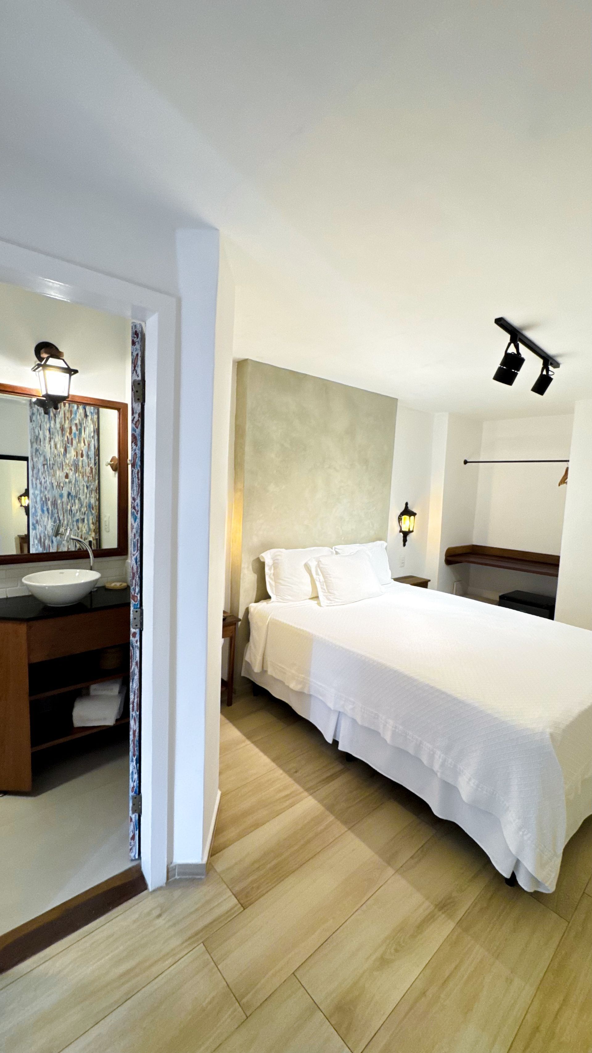 Bedroom with a white bed, beige walls, and bathroom partially visible.