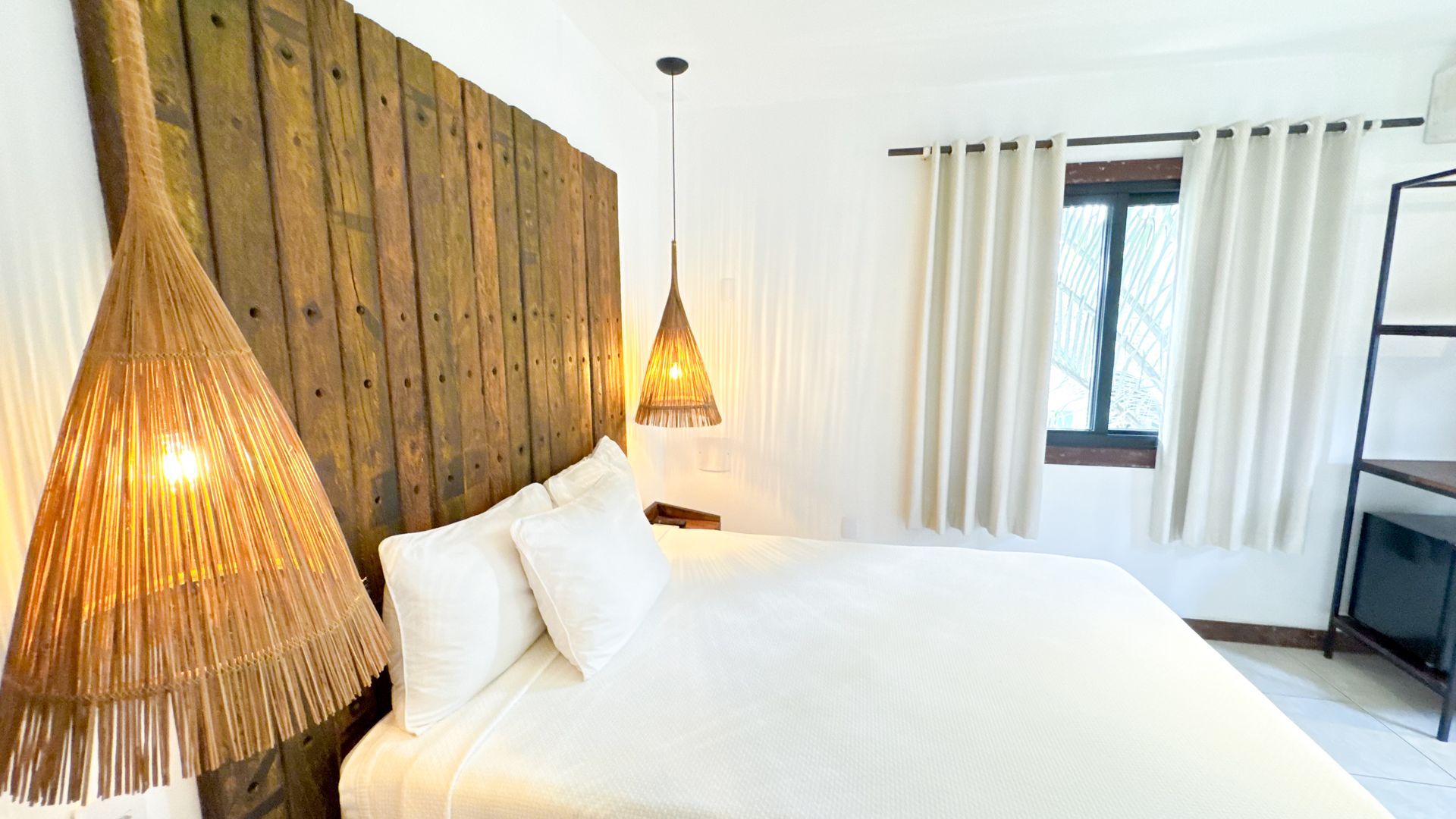 Bedroom with large wooden headboard, white bedding, and woven pendant lights.