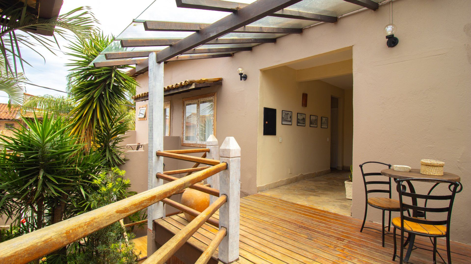 Balcony with wooden railing and glass roof, small table, chairs, and entry to building.