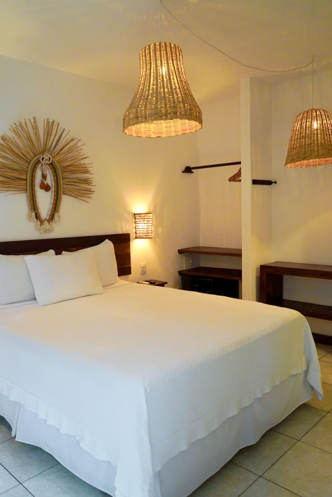 Bedroom with white linens, wooden headboard, woven lamps, and wall decor.