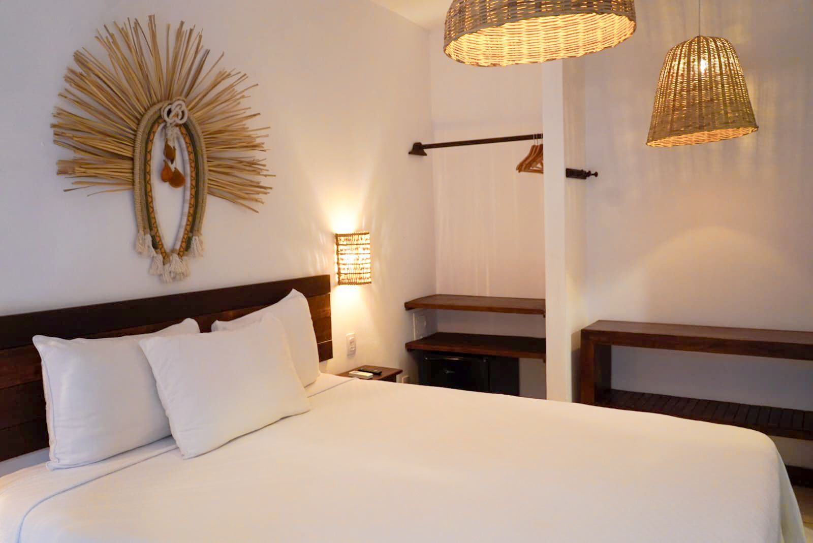 Bedroom with white bedding, wooden headboard, woven light fixtures, and wall art.