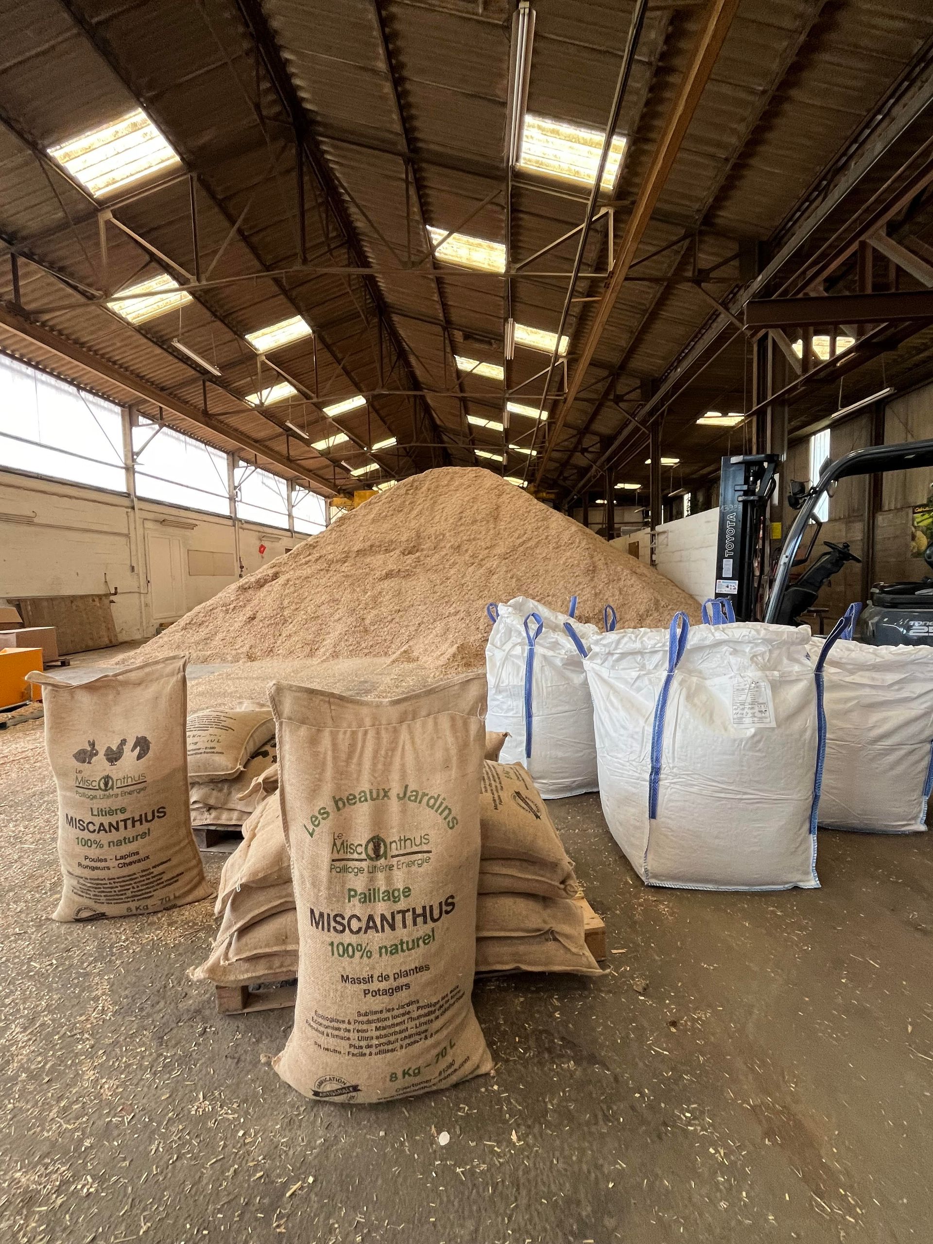 Un entrepôt rempli de sacs de copeaux de bois et d'un chariot élévateur.