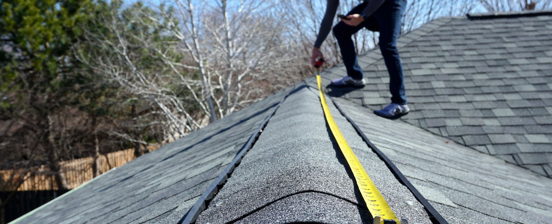 A man is measuring a roof with a tape measure.