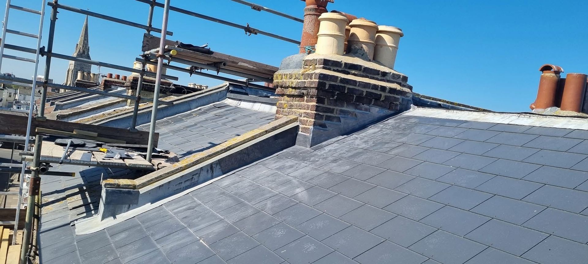 A roof with scaffolding and chimneys on it and a blue sky in the background.
