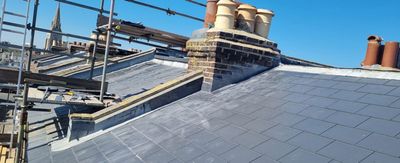 A roof with chimneys and scaffolding on it and a blue sky in the background.