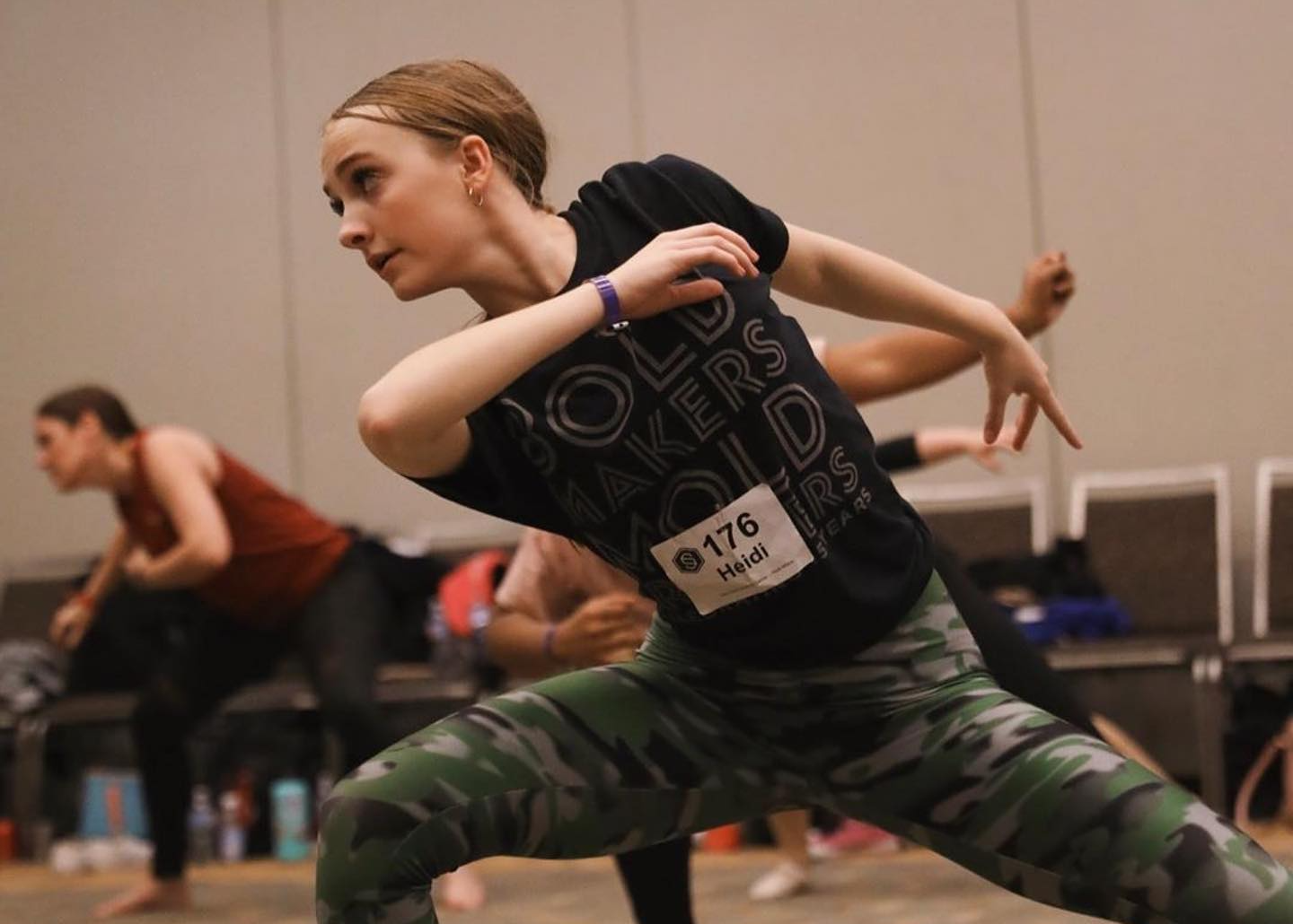 A woman in a black shirt and camo pants is dancing.