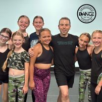A group of young girls are posing for a picture with a man in a dance studio.
