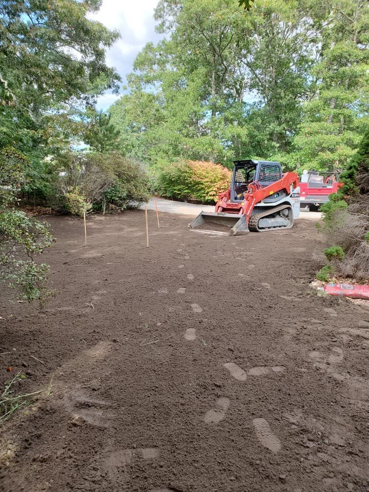 Mini excavator grading a dirt area near trees.