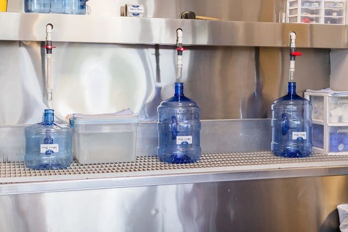 Three bottles of water are sitting on a shelf in a kitchen.