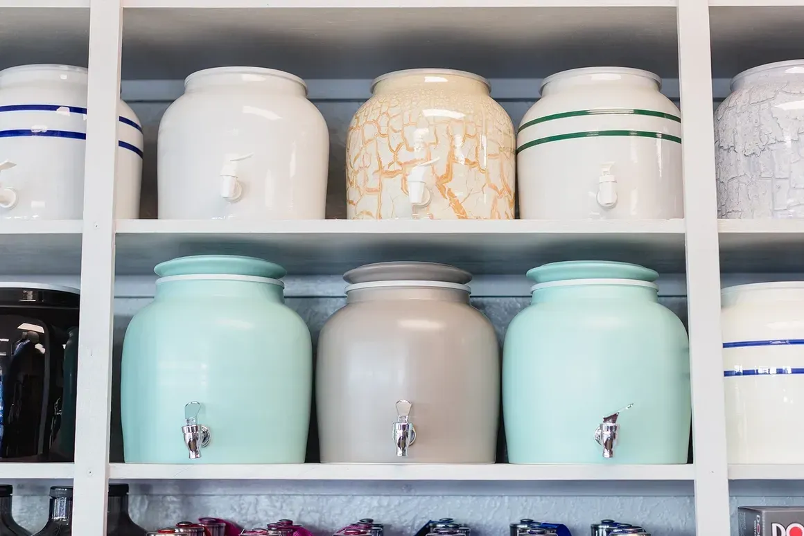 A shelf filled with lots of different colored jars with handles.