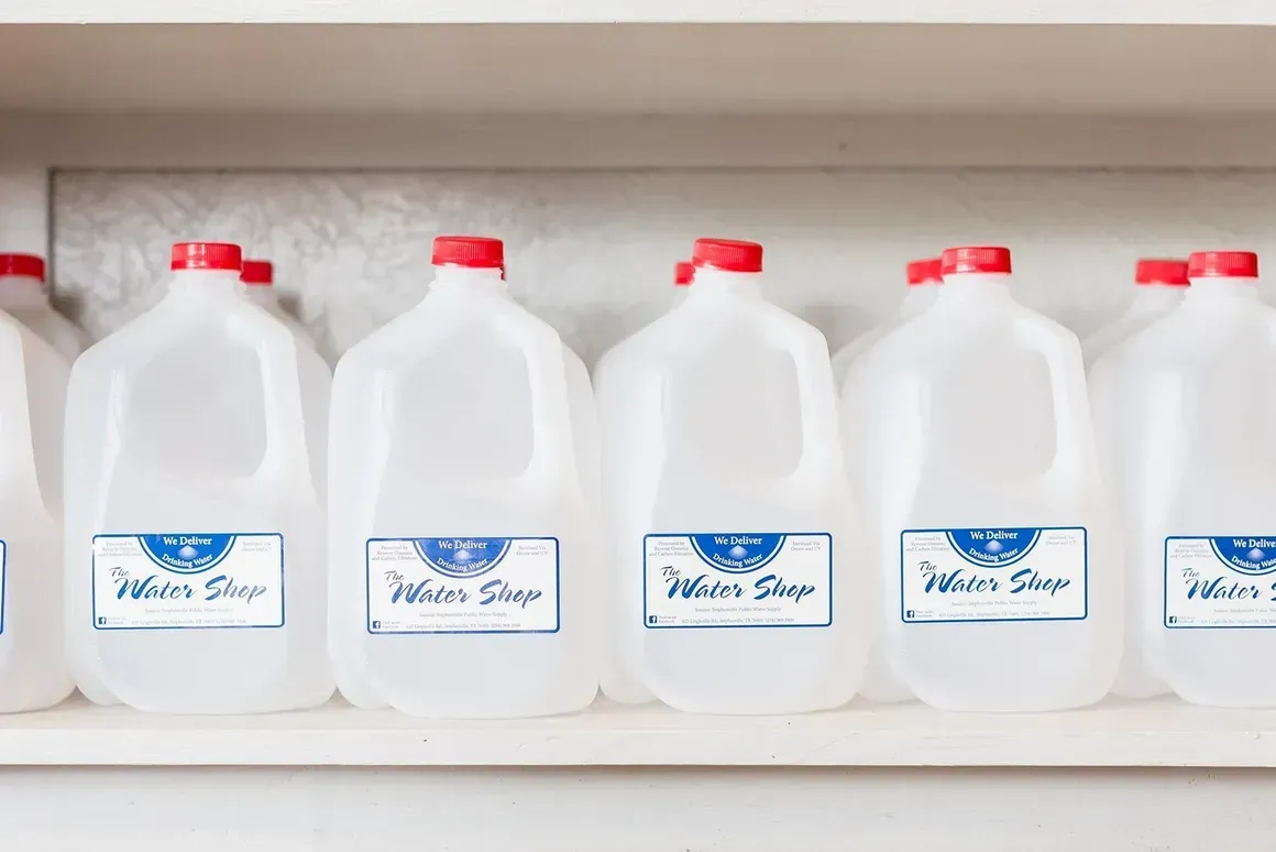 Several gallons of water are lined up on a shelf.