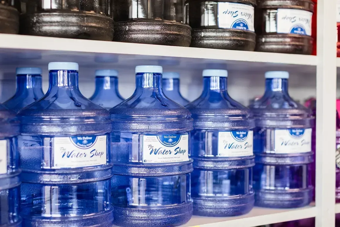 A row of water bottles are lined up on a shelf.
