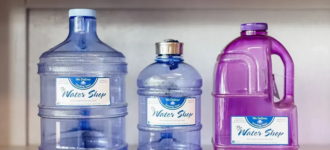 Three bottles of water are sitting on a shelf.