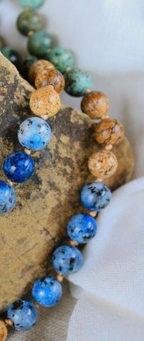 A close up of a bracelet with blue and brown beads on a rock.