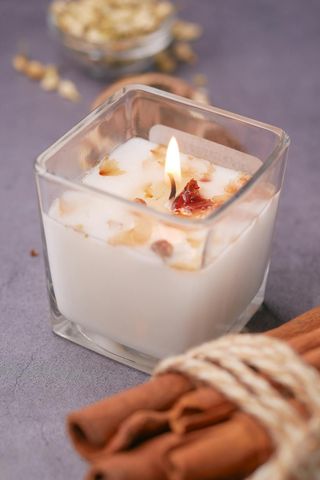 A candle is lit in a glass jar next to cinnamon sticks.