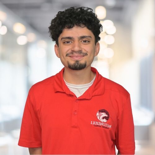 Man in red polo shirt with logo, smiling indoors.