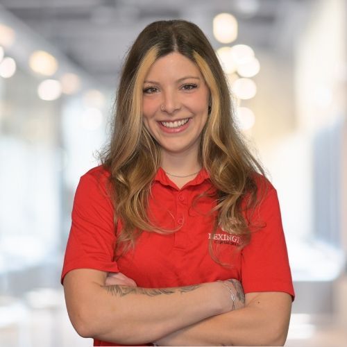 Woman with blonde streaks in red polo shirt smiling in office setting.