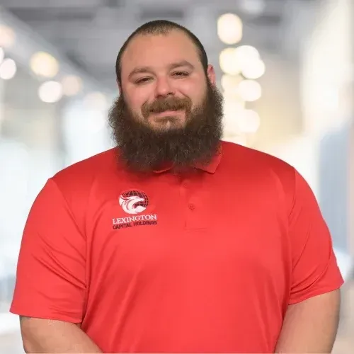 Man with a beard, smiling, arms crossed, wearing a light blue button-down shirt.