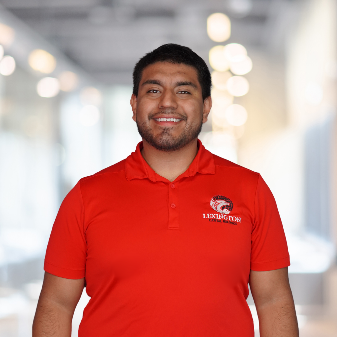 Man in red polo shirt with a logo, smiling in a well-lit office.