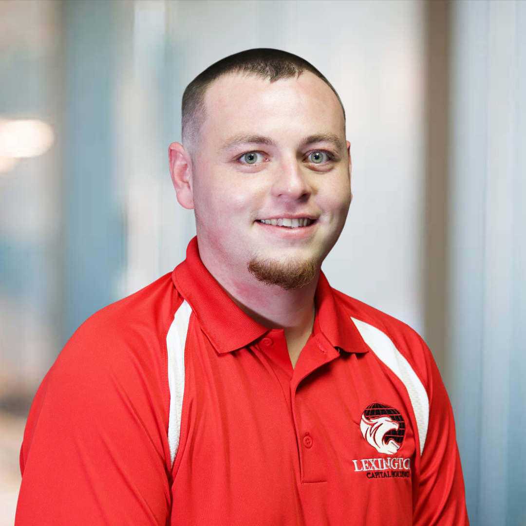 Man in red polo shirt, smiling, looking at the camera. Blurred background.