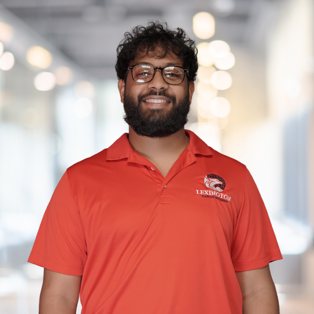 Man with glasses and beard wearing a red shirt smiles in front of a blurred background.