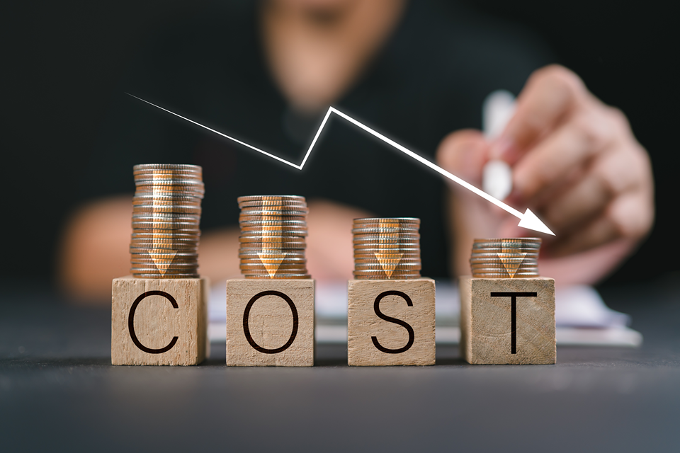 Stacks of coins placed on wooden blocks spelling out 'COST,' with a downward-sloping white arrow symbolizing cost reduction and better efficiency