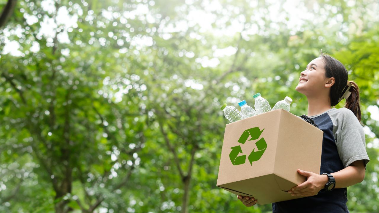 A woman is holding a cardboard box with a recycling symbol on it.