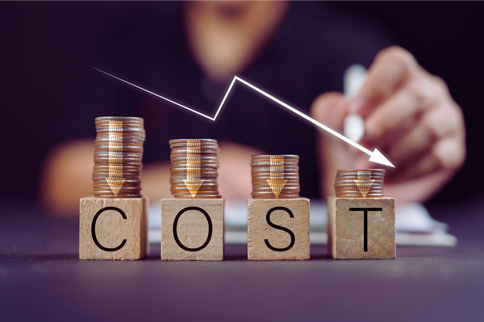 A person is stacking coins on wooden blocks with the word cost written on them.