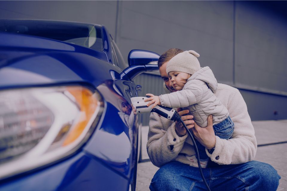 A man is holding a baby while charging an electric car.