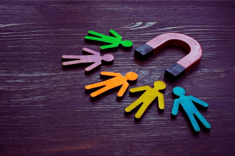 Colorful wooden figures representing people being attracted to a red horseshoe magnet on a dark wooden surface