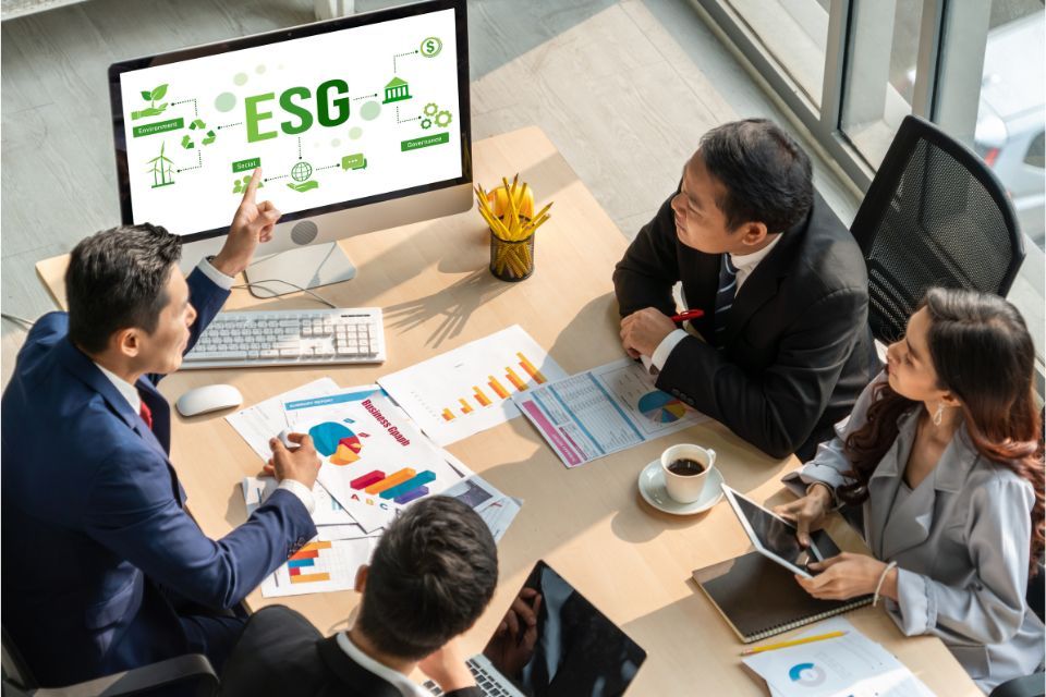 Business professionals in a meeting discussing ESG strategies, with charts and documents on the table and an ESG presentation displayed on a computer screen