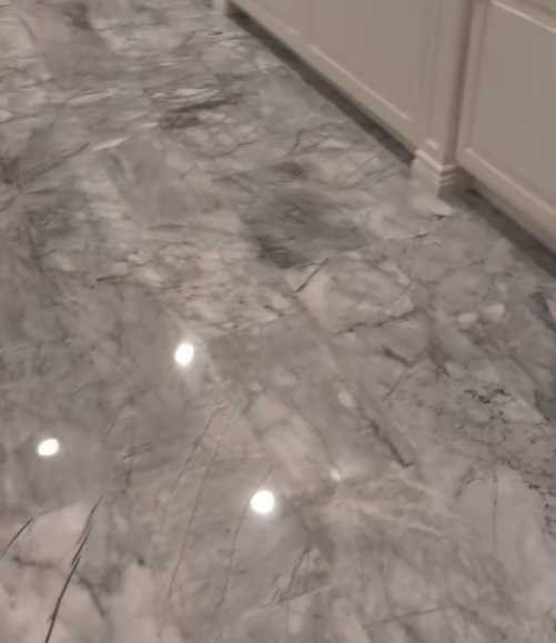 Gray and white marbled flooring with white cabinets along the wall.