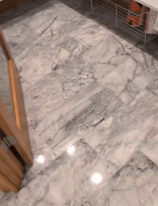 Marble flooring with gray veining and recessed lights. Wooden door frame on the left.