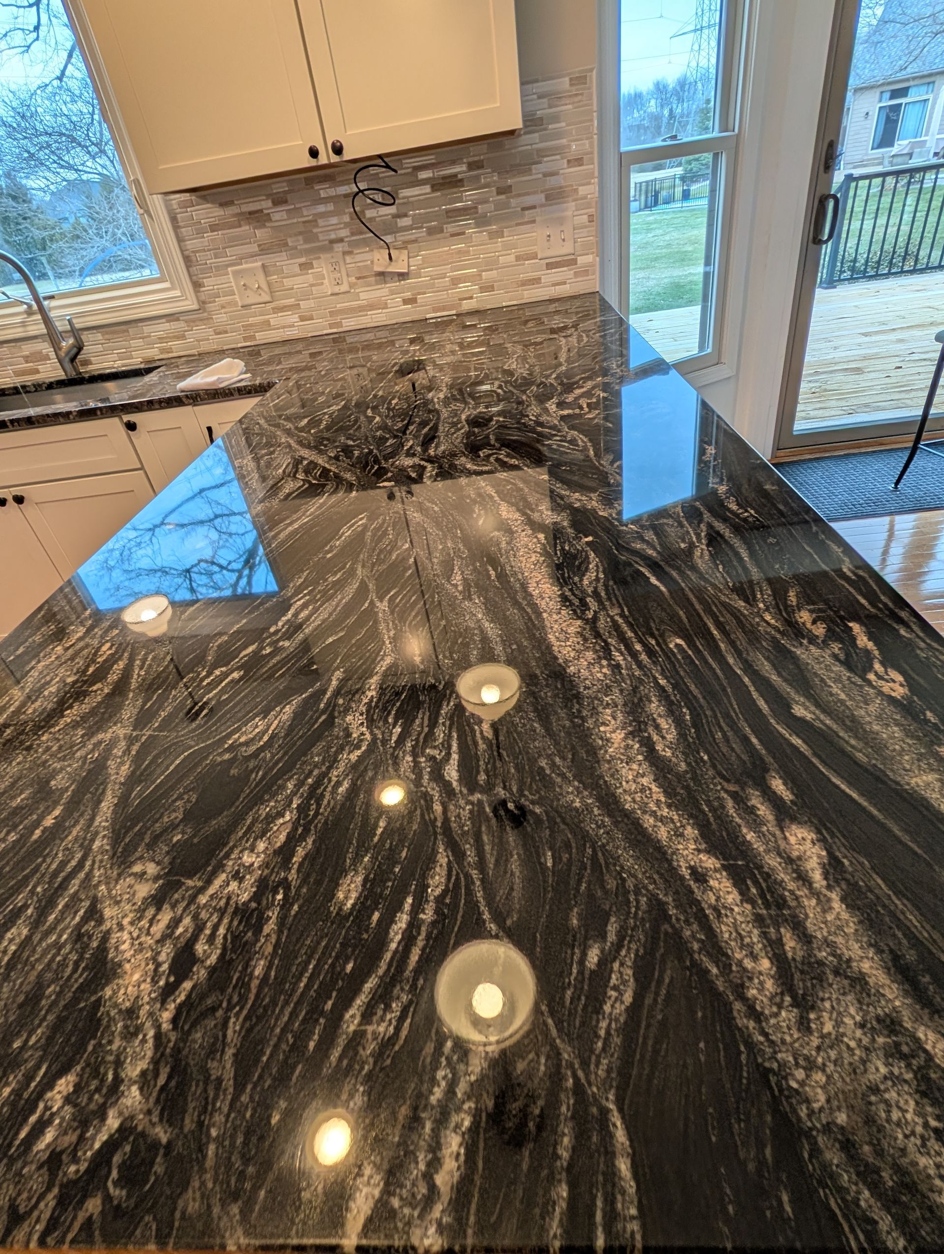 A high-angle view of a kitchen island with black and white veined granite countertops and three small glass candle holders.
