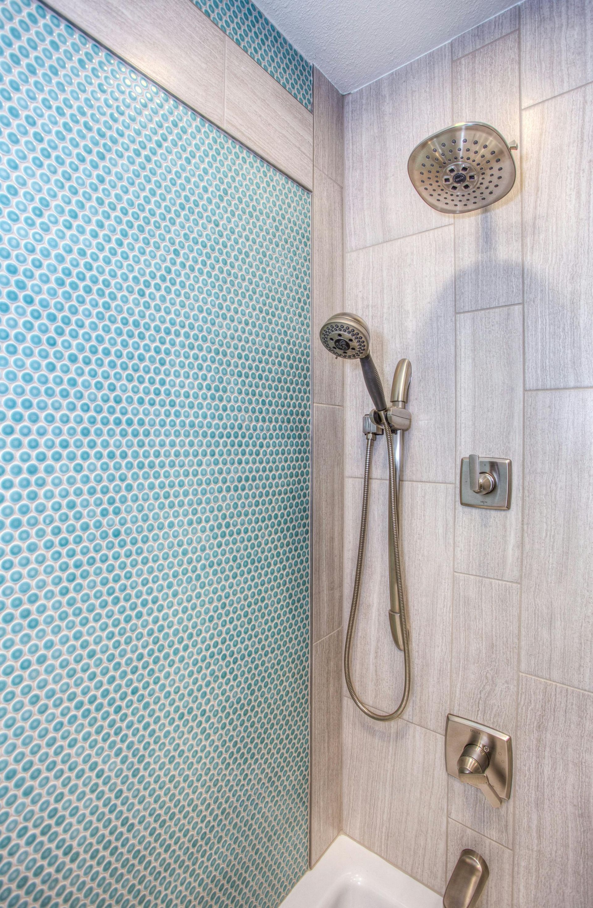 Shower stall with teal mosaic tile wall and gray tile, two shower heads, and fixtures.