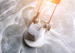 Floor polishing machine working on a light-colored surface, possibly concrete.