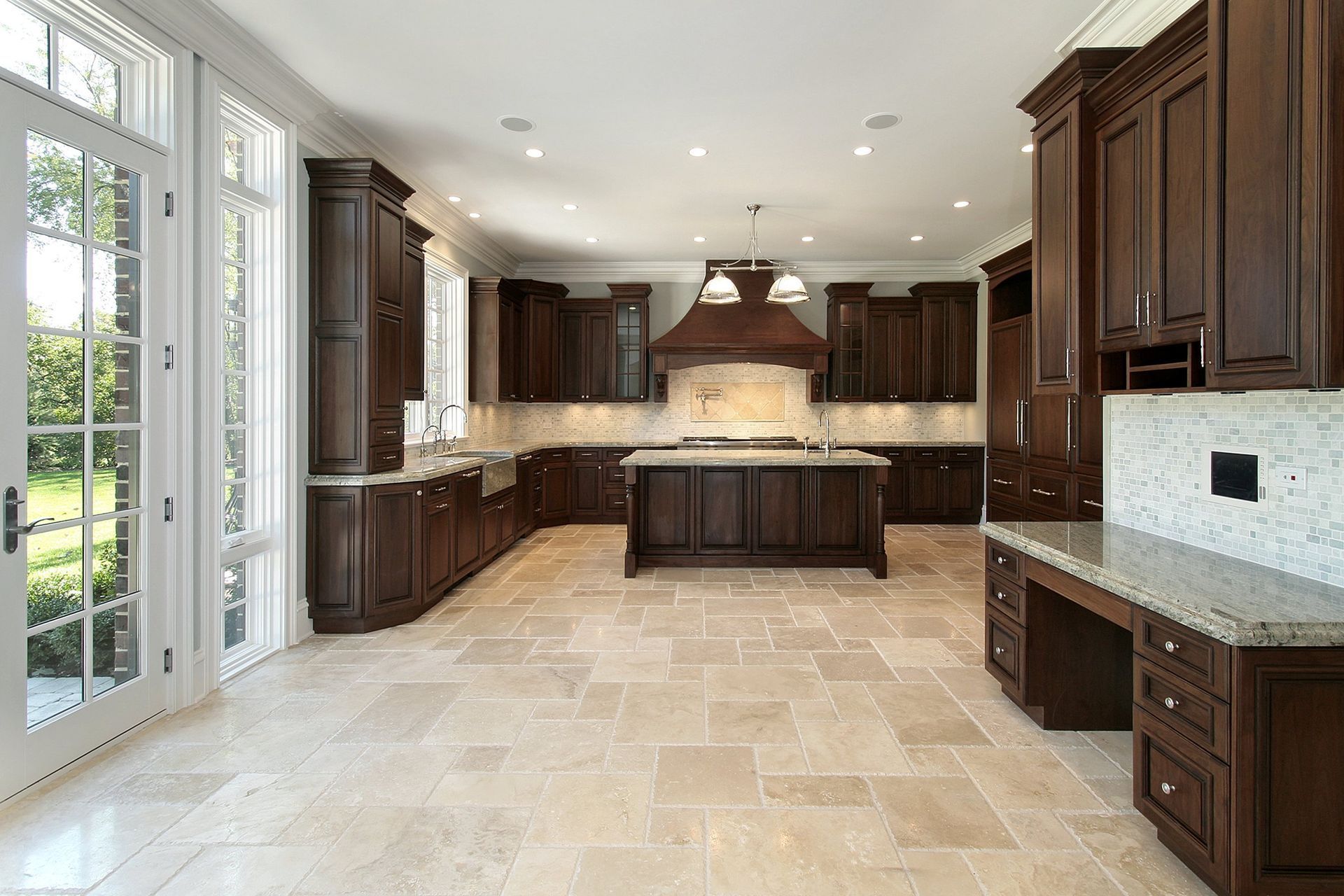 Spacious kitchen with dark wood cabinets, center island, light stone floor, and glass doors.